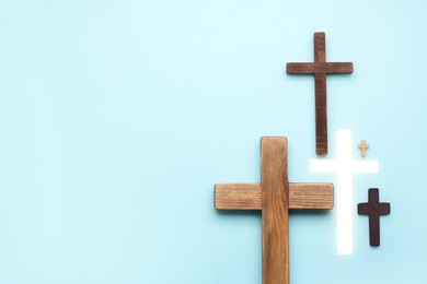 Photo of Many different crosses on light blue background, flat lay with space for text. Religion of Christianity