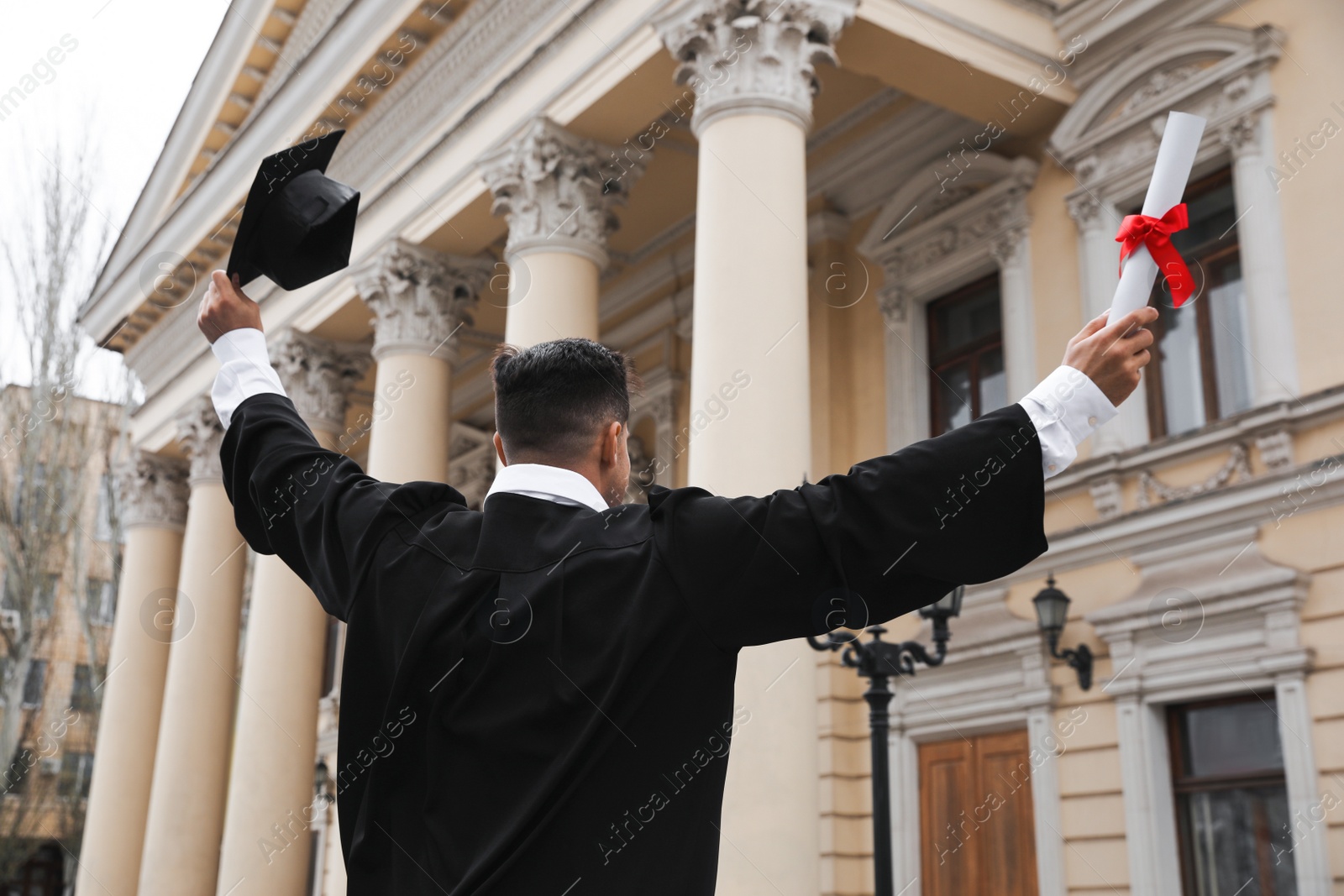 Photo of Student with diploma after graduation ceremony outdoors, back view