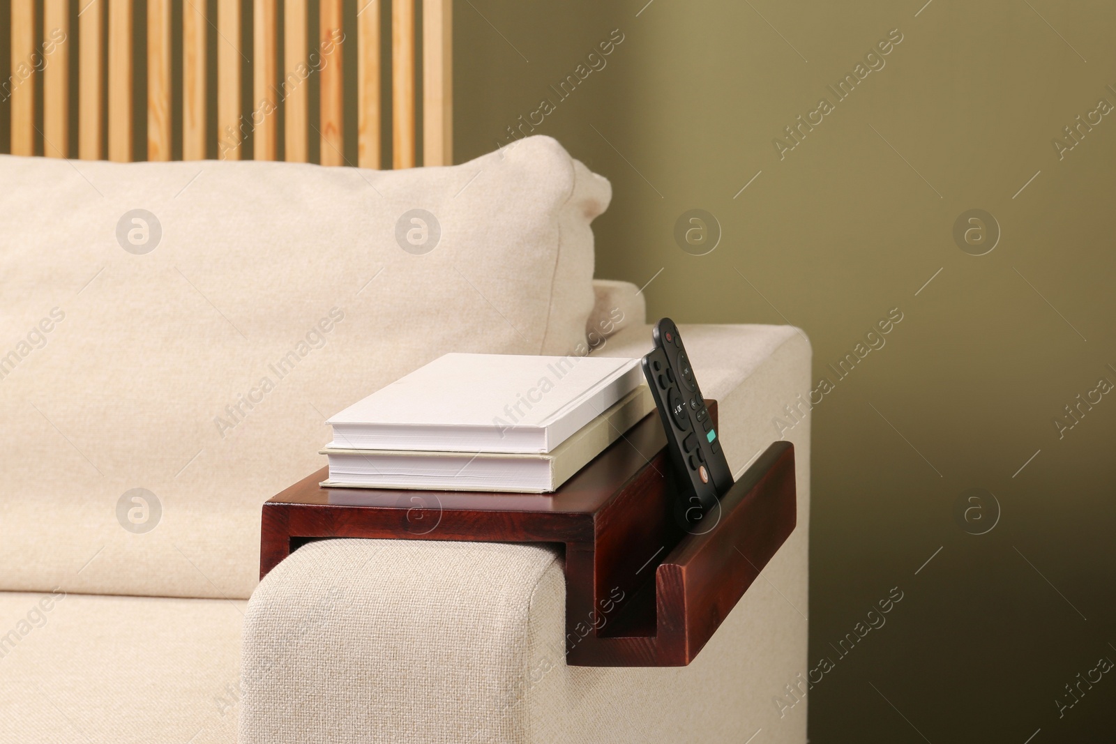 Photo of Books and remote controls on sofa armrest wooden table in room. Interior element