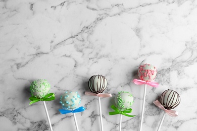 Different tasty cake pops on white marble background, flat lay. Space for text