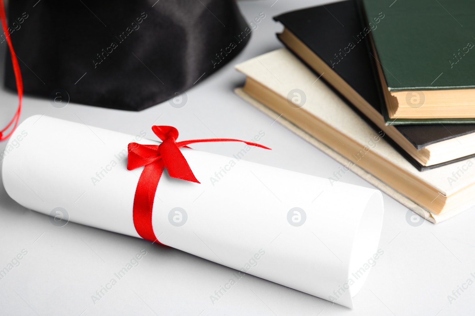 Photo of Graduation hat, books and student's diploma on white background