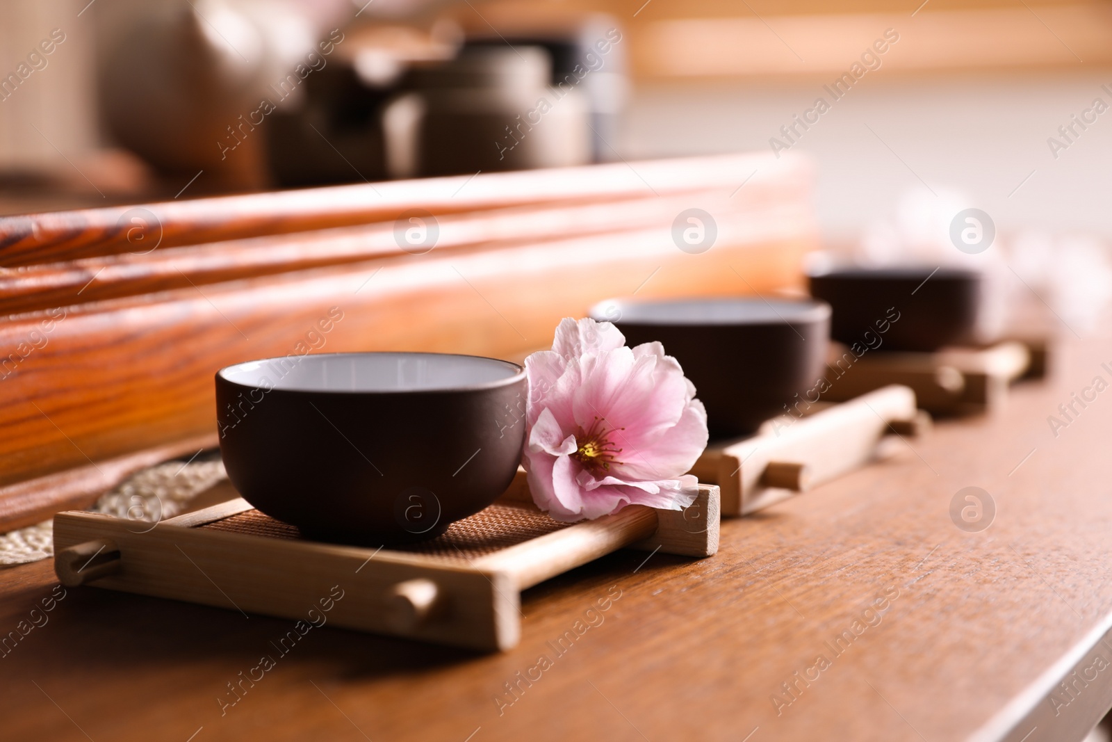 Photo of Cup with sakura flower for traditional tea ceremony on wooden table, closeup