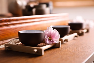 Photo of Cup with sakura flower for traditional tea ceremony on wooden table, closeup