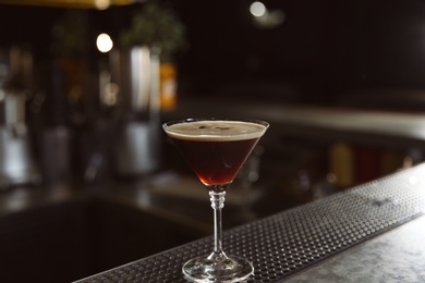 Photo of Glass of martini espresso cocktail on bar counter, closeup. Space for text