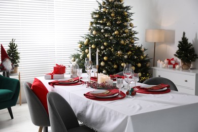 Photo of Christmas table setting with burning candles, gift box and dishware in room