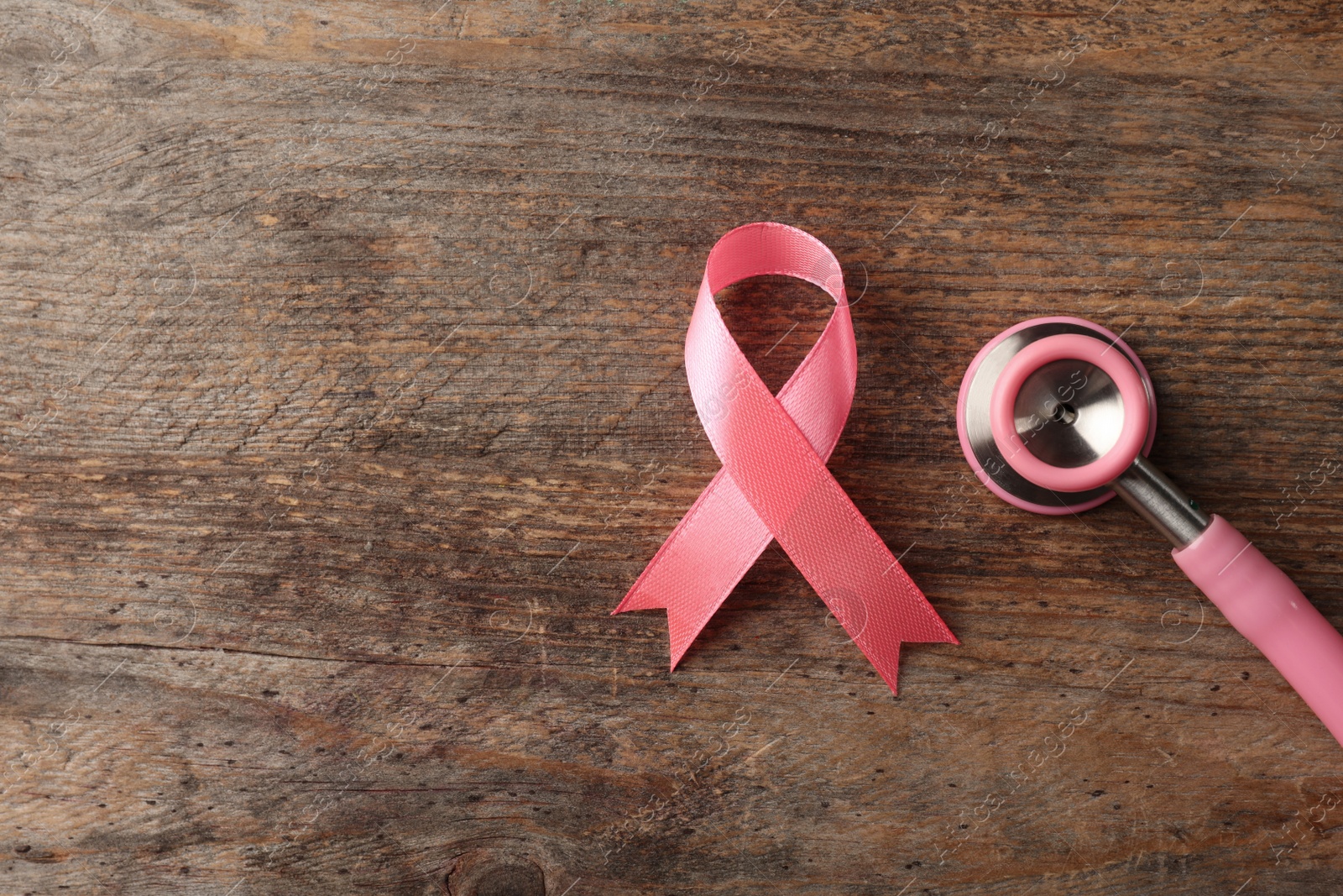 Photo of Pink ribbon and stethoscope on wooden background, top view with space for text. Breast cancer concept