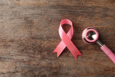 Photo of Pink ribbon and stethoscope on wooden background, top view with space for text. Breast cancer concept