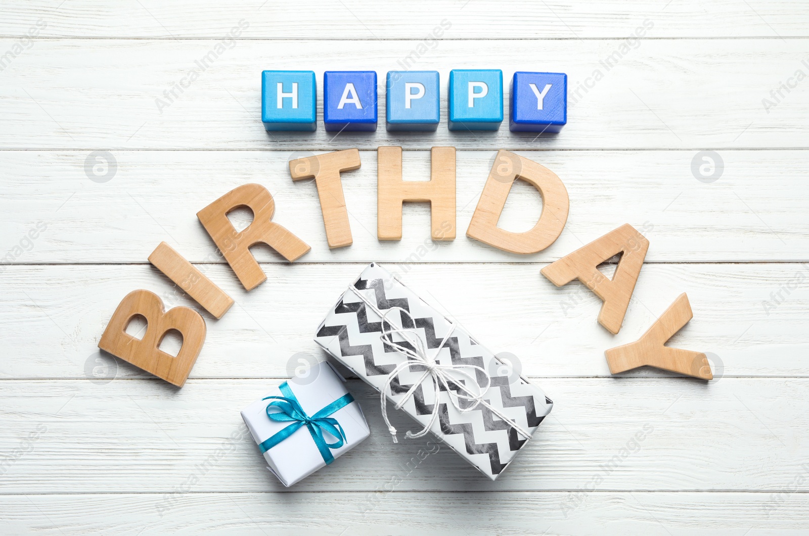 Photo of Flat lay composition with words HAPPY BIRTHDAY and gift boxes on white wooden background