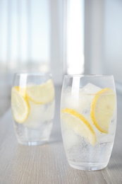 Photo of Soda water with lemon slices and ice cubes on wooden table indoors