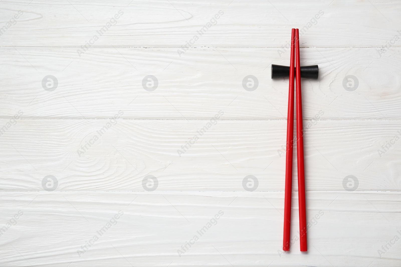 Photo of Pair of red chopsticks with rest on white wooden table, top view. Space for text