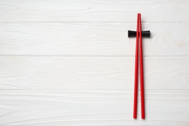 Photo of Pair of red chopsticks with rest on white wooden table, top view. Space for text