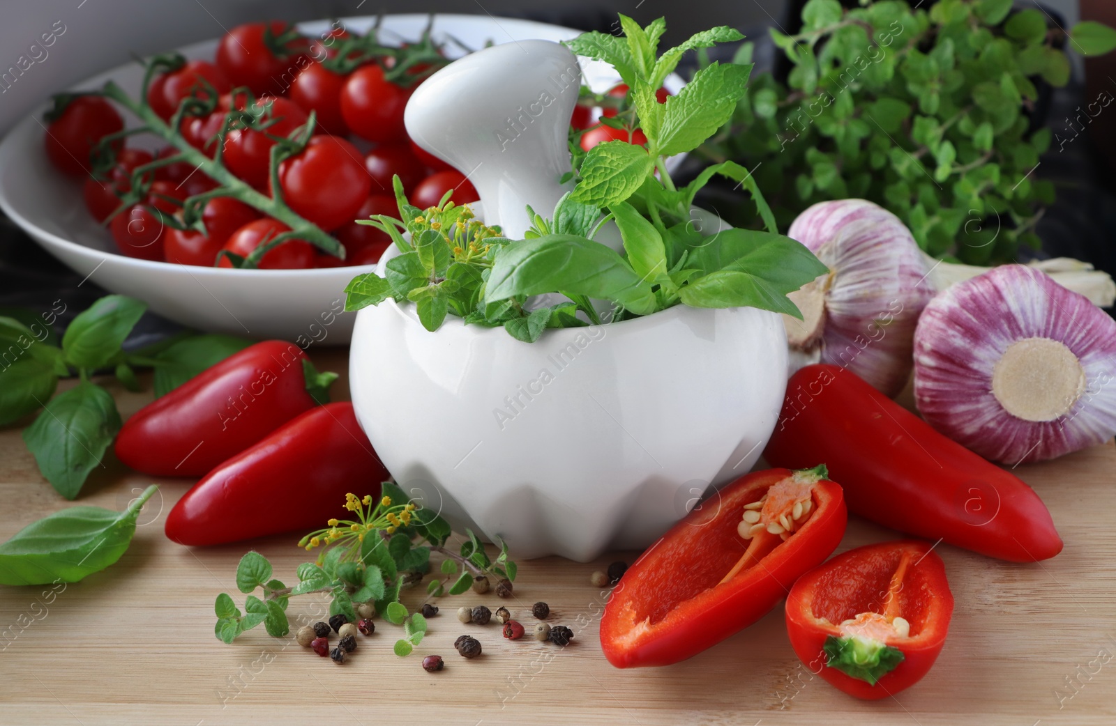 Photo of Mortar with fresh herbs near garlic, pepper and cherry tomatoes on wooden table, closeup