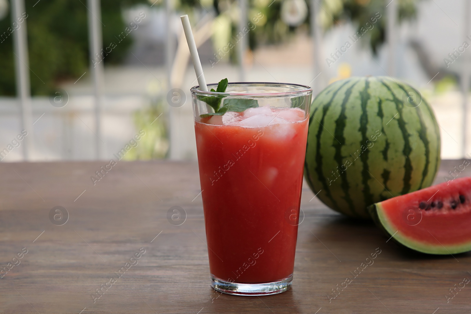 Photo of Glass of delicious watermelon drink with mint, ice cubes and fresh fruits on wooden table outdoors, space for text