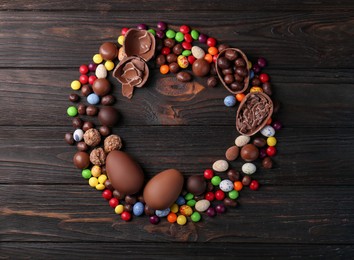 Photo of Frame made of tasty chocolate eggs and sweets on wooden table, flat lay. Space for text