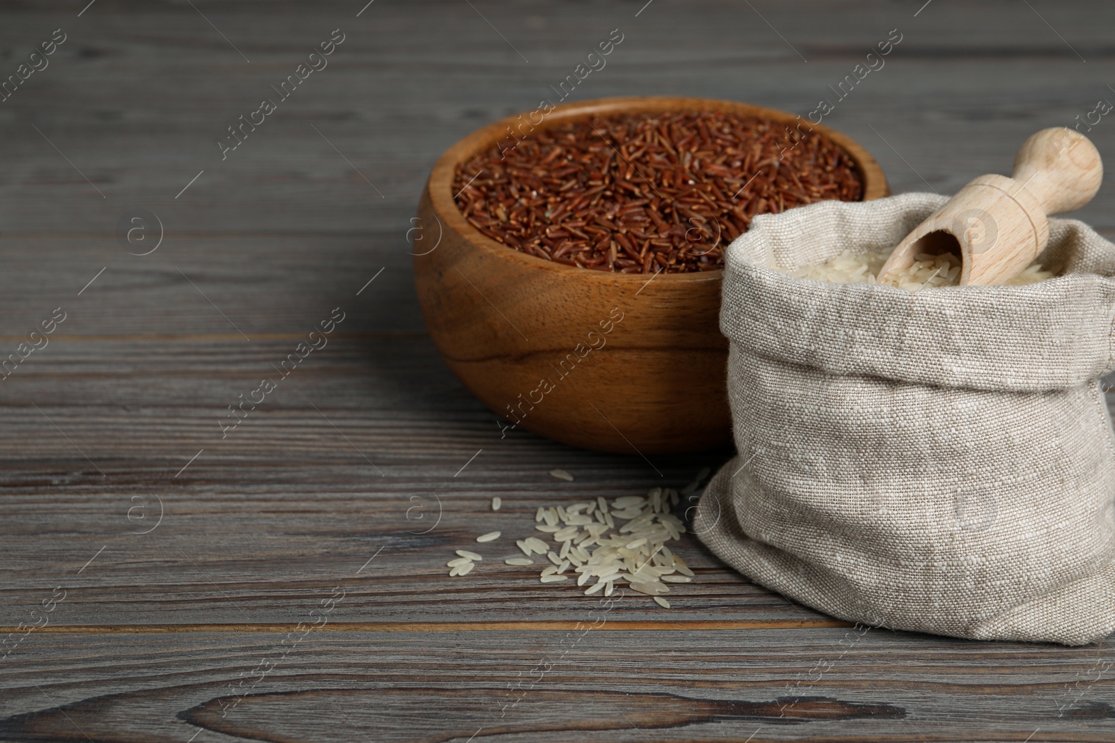 Photo of Bag and bowl with different sorts of rice on wooden table. Space for text