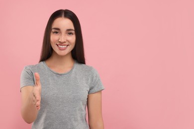 Photo of Happy young woman welcoming and offering handshake on pink background, space for text
