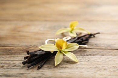 Photo of Beautiful vanilla flowers and sticks on wooden table, closeup