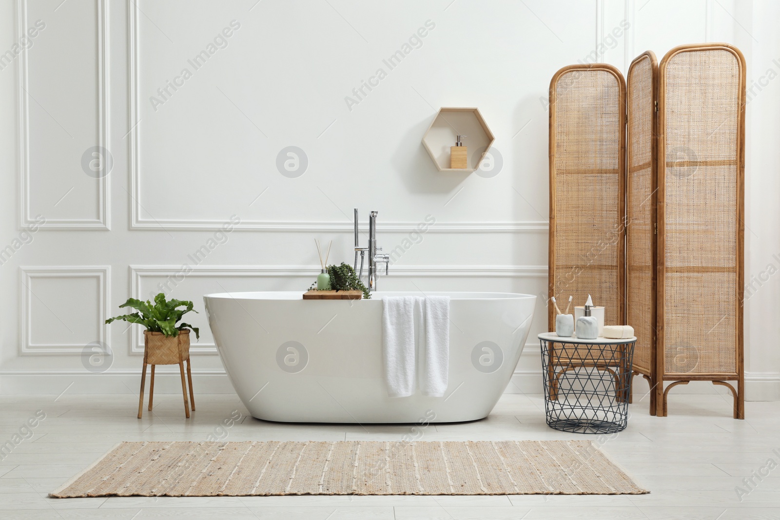 Photo of Modern ceramic bathtub and green plants near white wall in room