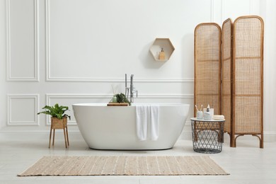 Modern ceramic bathtub and green plants near white wall in room