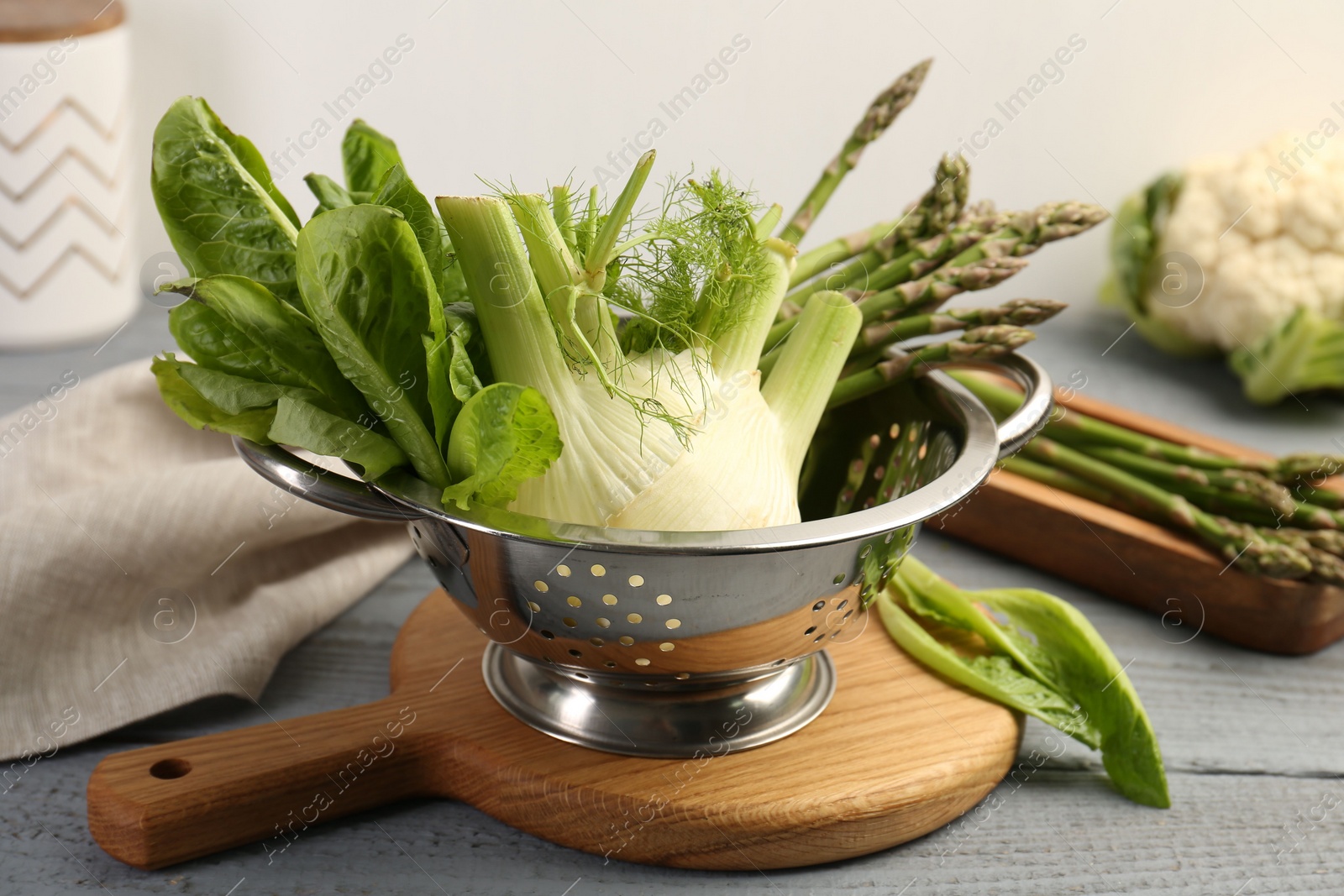 Photo of Metal colander with fennel, lettuce and asparagus on gray wooden table