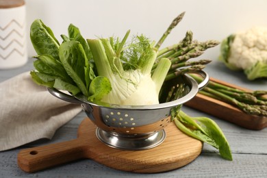 Photo of Metal colander with fennel, lettuce and asparagus on gray wooden table