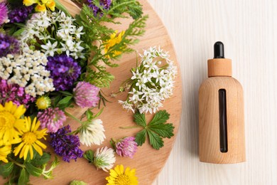 Flat lay composition with bottle of essential oil, flowers and herbs on white wooden table