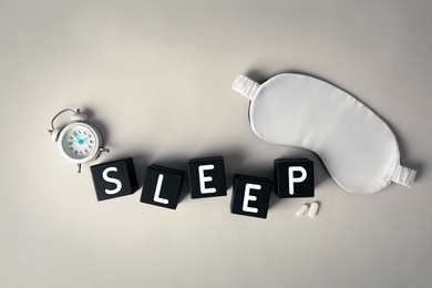 Photo of Word Sleep, alarm clock, pills and mask on light grey table, flat lay. Insomnia treatment