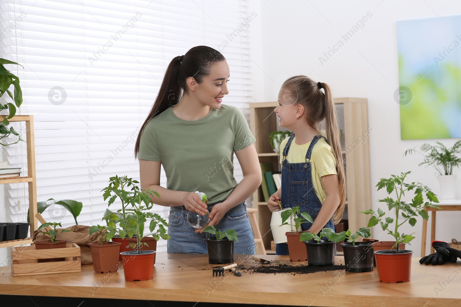 Photo of Mother and daughter taking care of seedlings together at wooden table in room
