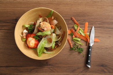 Photo of Peels of fresh vegetables and knife on wooden table, flat lay