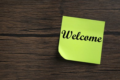 Sticky note with word Welcome on wooden table, top view. Space for text