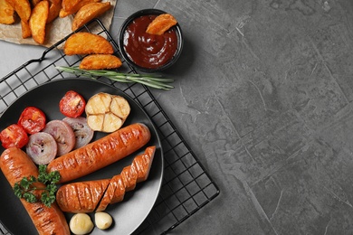 Delicious grilled sausages and vegetables on grey table, flat lay. Space for text