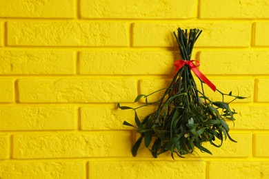Photo of Mistletoe bunch with red bow hanging on yellow brick wall, space for text. Traditional Christmas decor