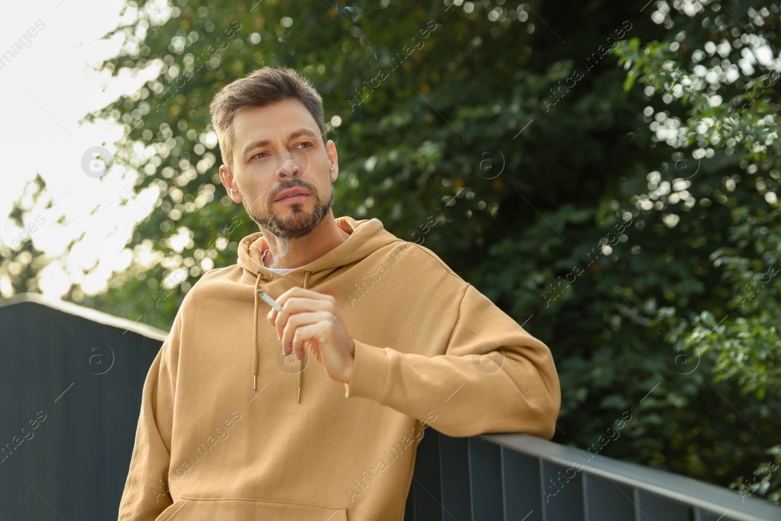 Photo of Man smoking cigarette near railing outdoors. Bad habit