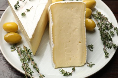 Photo of Plate with pieces of tasty camembert cheese, olives and rosemary on table, closeup