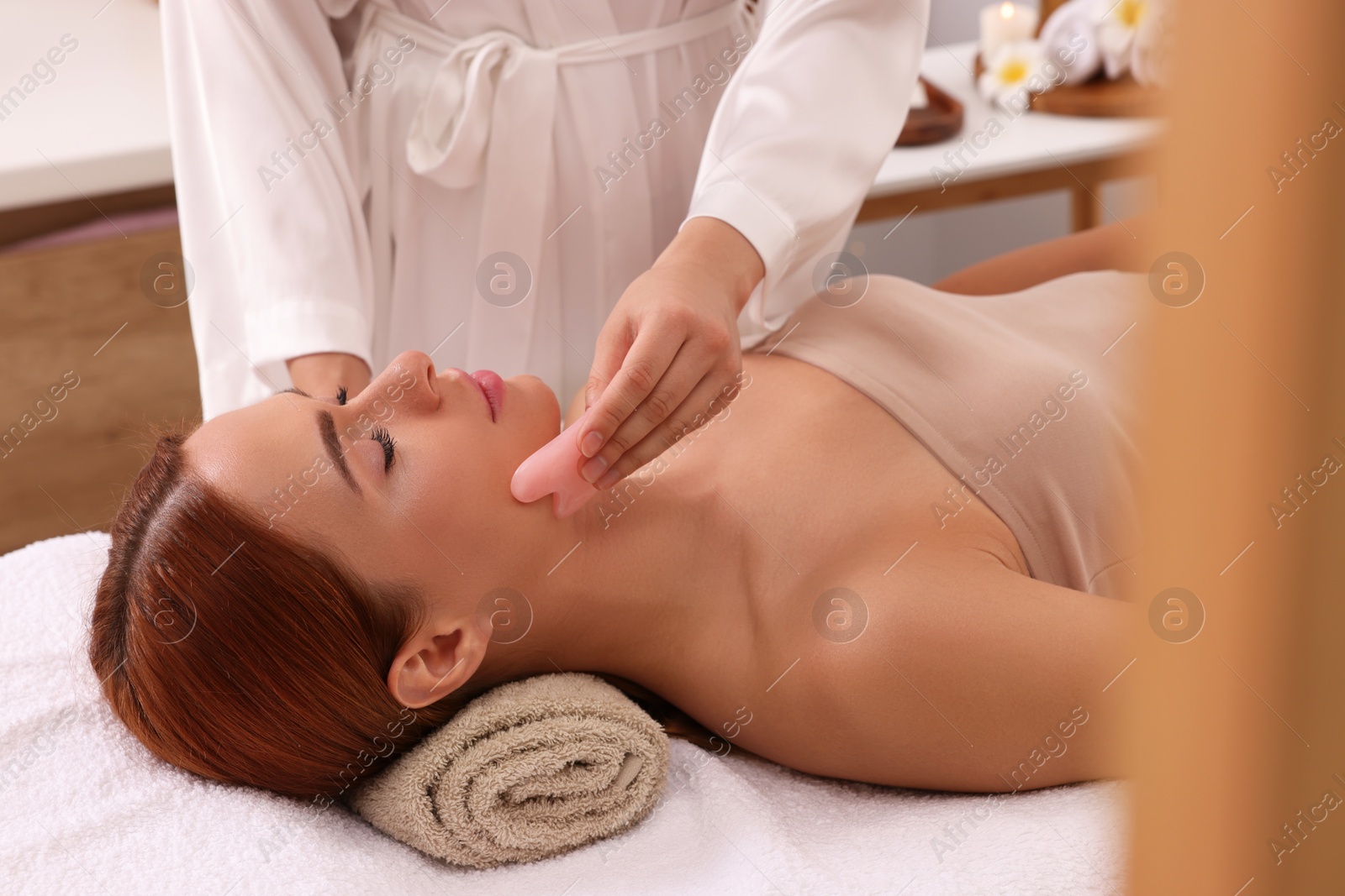 Photo of Young woman receiving facial massage with rose quartz gua sha tool in beauty salon, closeup