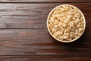 Photo of Delicious pearl barley in bowl on wooden table, top view. Space for text