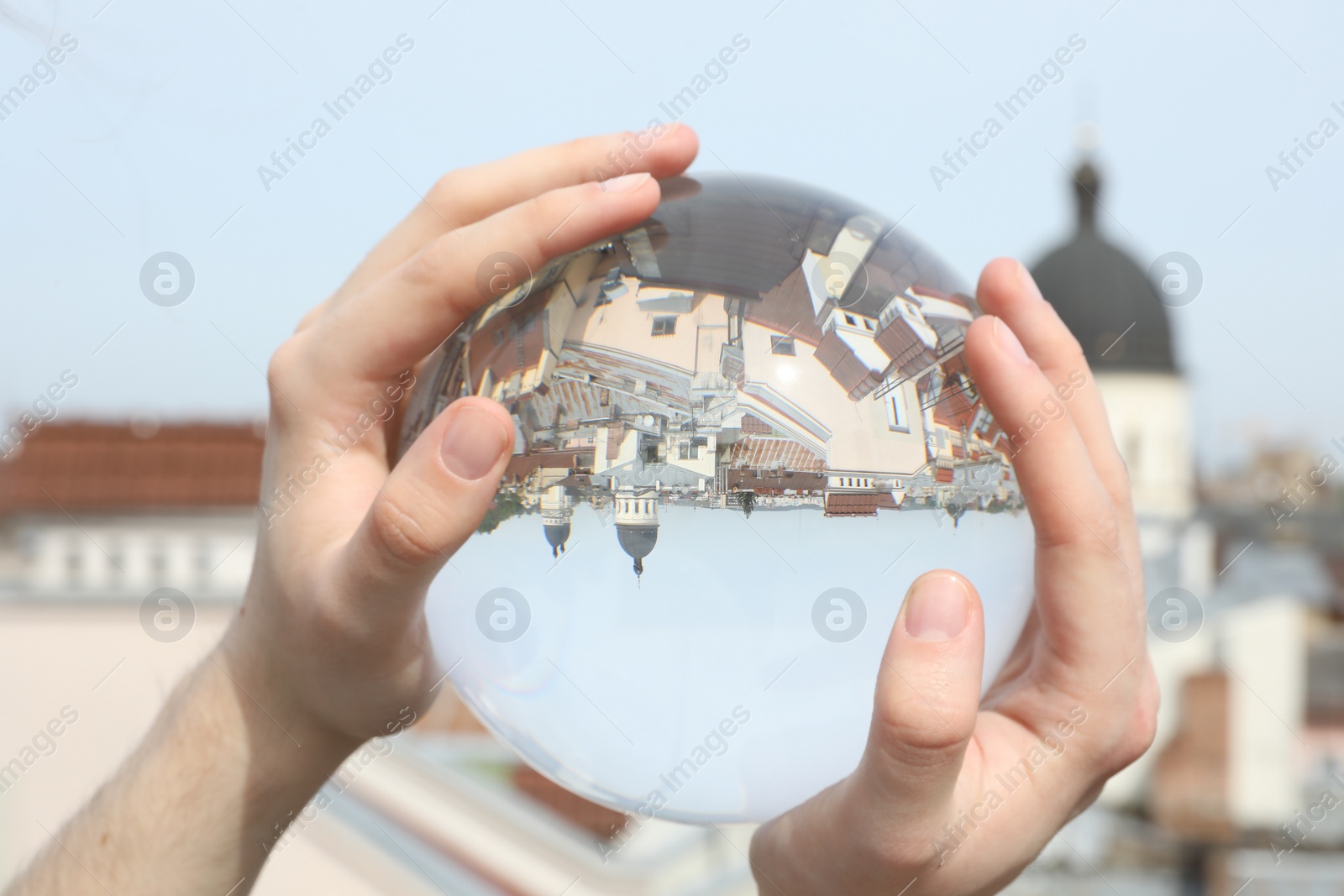 Photo of View of beautiful city street, overturned reflection. Man holding crystal ball outdoors, closeup