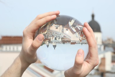 View of beautiful city street, overturned reflection. Man holding crystal ball outdoors, closeup