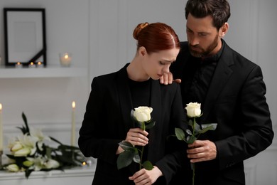 Photo of Sad couple with white roses mourning indoors. Funeral ceremony