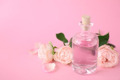 Photo of Bottle of essential oil and roses on pink background