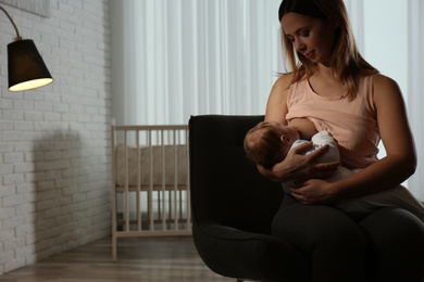 Photo of Young woman breast feeding her little baby at home. Space for text