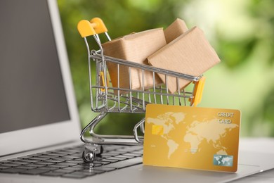 Online payment concept. Small shopping cart with bank card, boxes on laptop, closeup