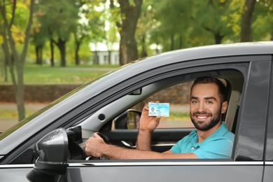 Young man holding driving license in car