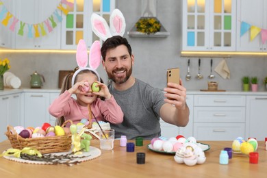 Father with his cute daughter making selfie at table in kitchen. Painting Easter eggs