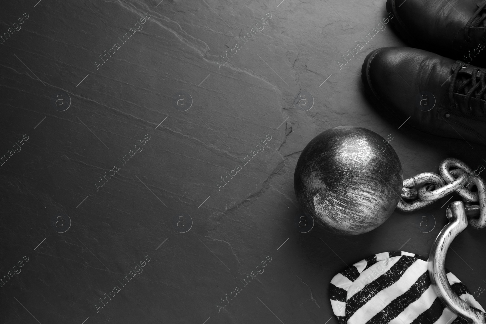 Photo of Prisoner ball with chain, jail cap and boots on black table, flat lay. Space for text