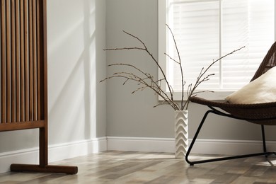 Photo of Beautiful tree twigs in vase on floor and chair near window indoors