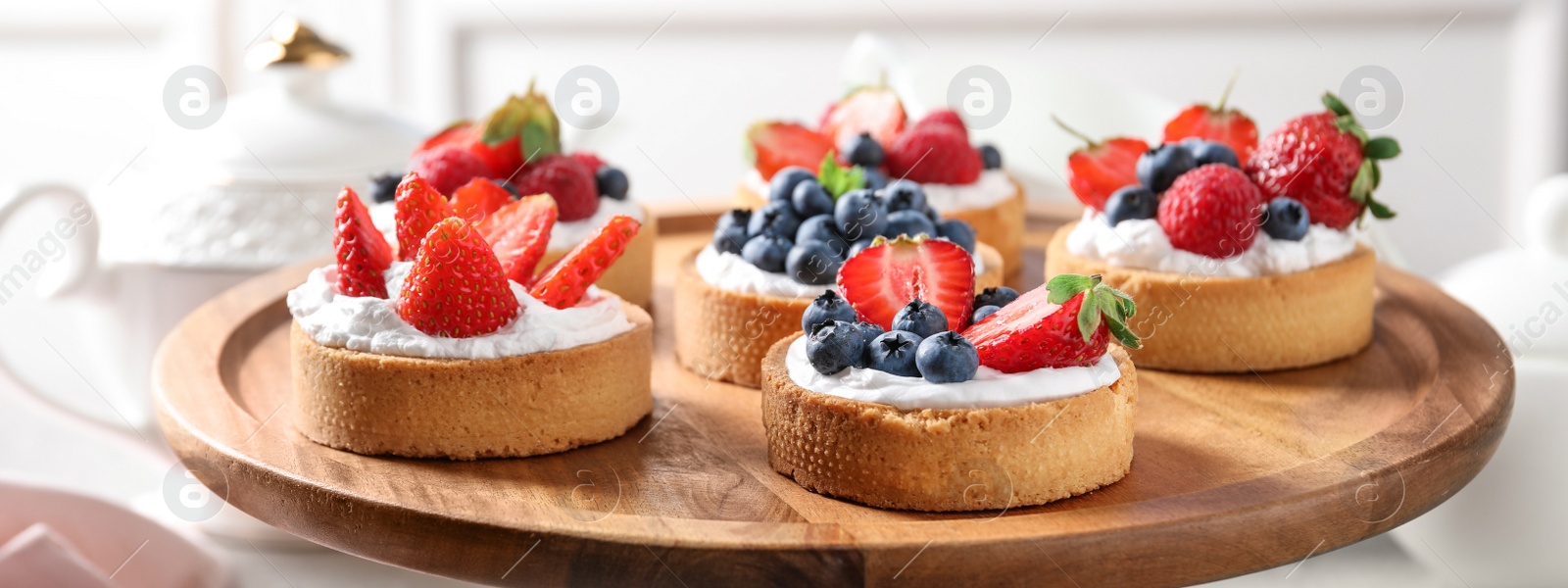 Image of Tasty tartlets with fresh berries on cake stand, closeup. Banner design