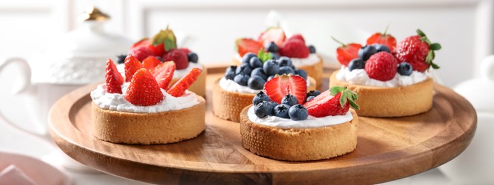 Tasty tartlets with fresh berries on cake stand, closeup. Banner design