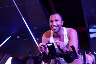 Photo of Young man training on exercise bike in fitness club. Space for text