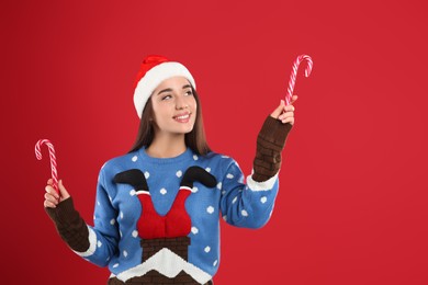 Photo of Young woman in Christmas sweater and Santa hat holding candy canes on red background